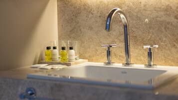 Ein Badezimmerwaschbecken mit einem modernen Wasserhahn, einer Marmorarbeitsplatte und drei Seifenspendern.