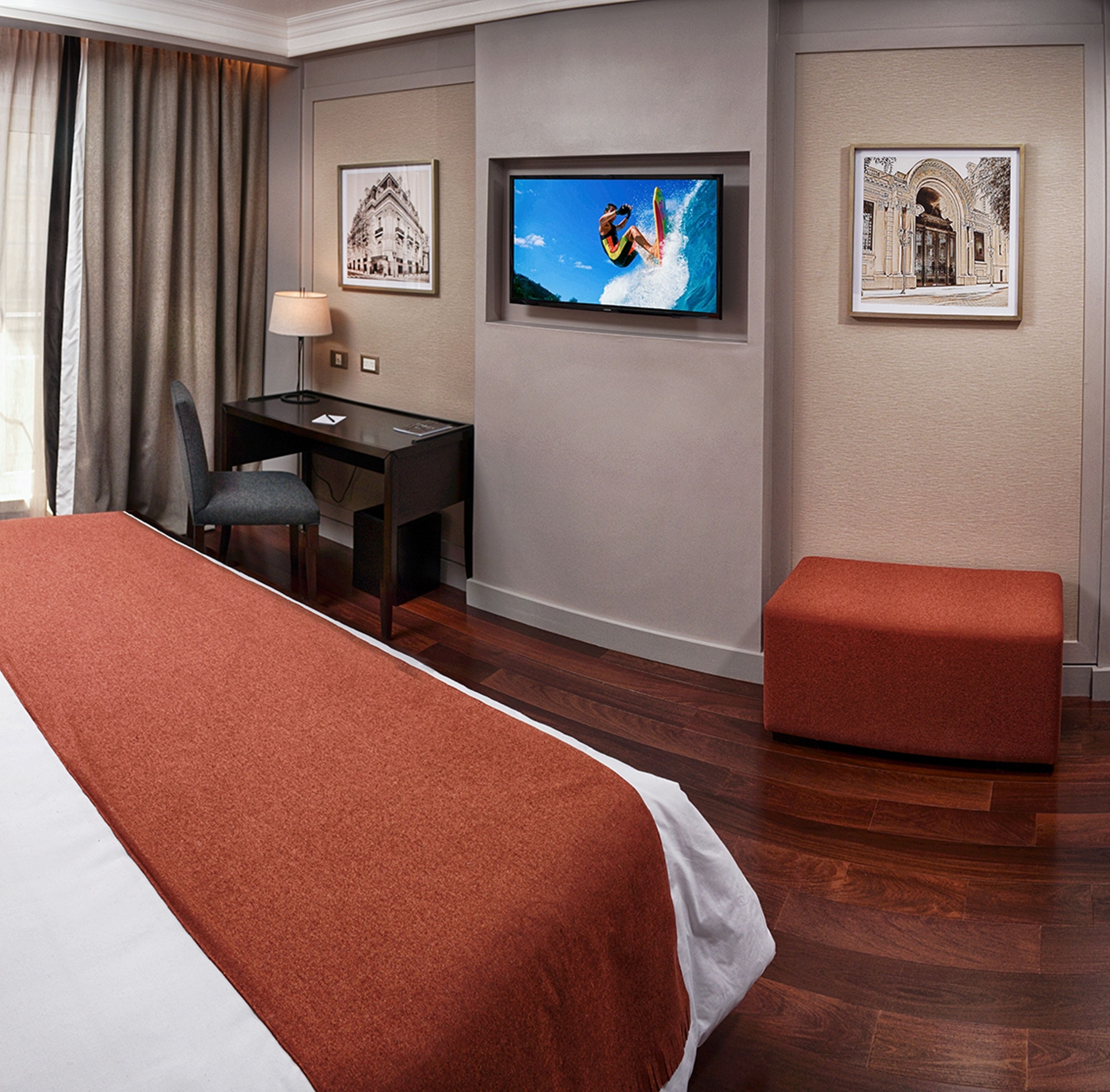 Ein Hotelzimmer mit einem Bett, einem Schreibtisch, einem Fernseher und zwei gerahmten Bildern an der Wand.