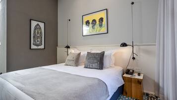 A neatly made bed with a gray blanket, a bedside table with a phone and a lamp, and two framed artworks on the wall.