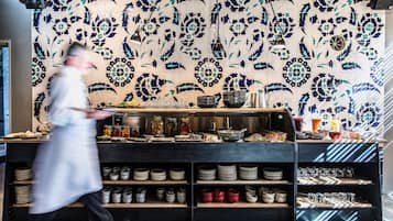 A kitchen with a tiled backsplash, shelves with plates and bowls, and a counter with food items.