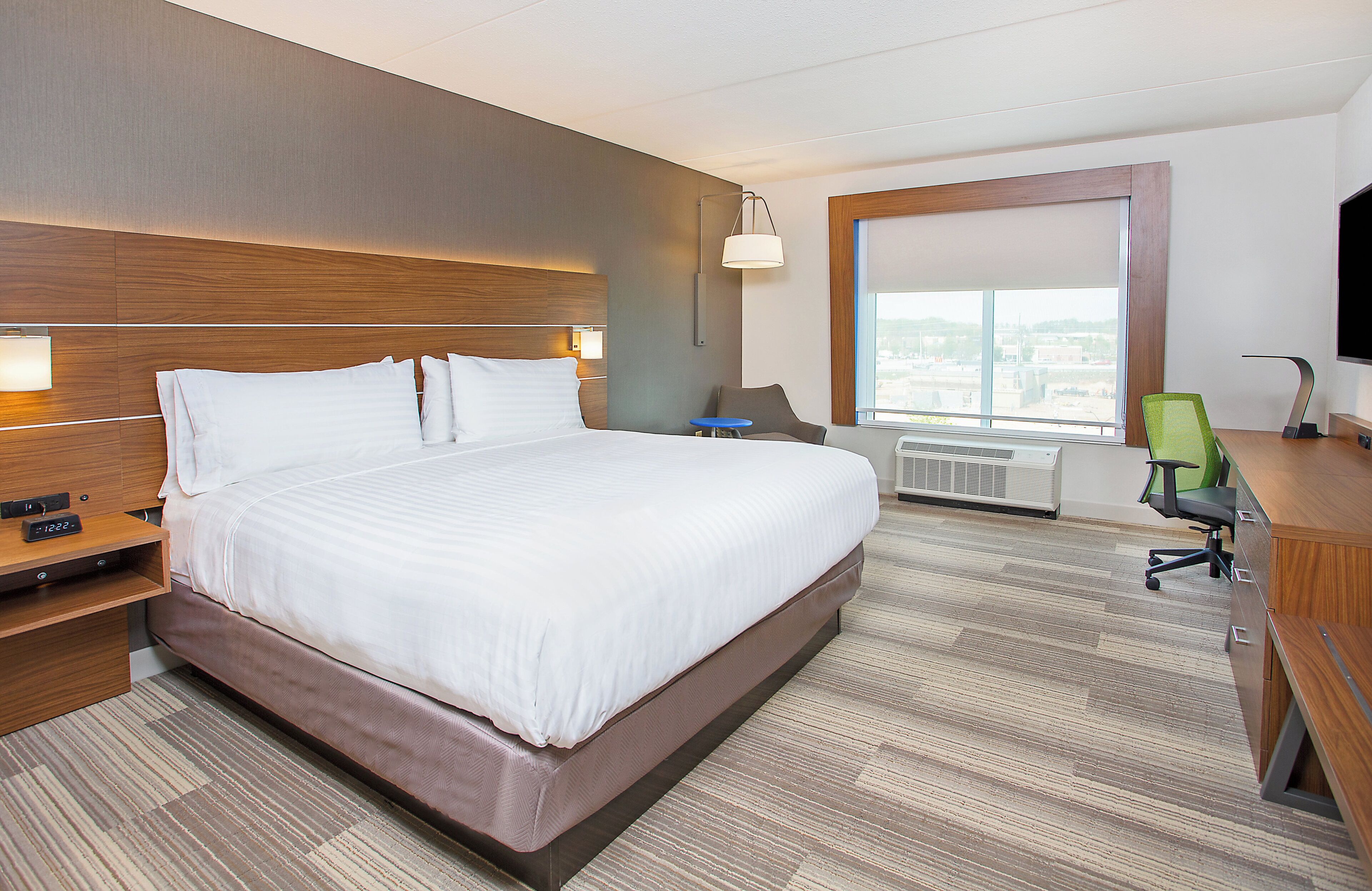 A hotel room with a large bed, bedside tables, a desk with a chair, a TV, and a large window.