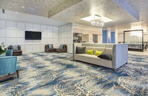 A spacious lobby with a large sofa, two armchairs, a flat-screen TV, and a patterned carpet.