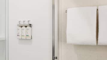 A bathroom with a shower, a towel rack with two towels, and three Dove shampoo bottles on a wall-mounted dispenser.