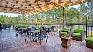 An outdoor patio with wooden beams, wicker furniture, and a view of trees. - Holiday Inn Express & Suites Covington by IHG (Covington)