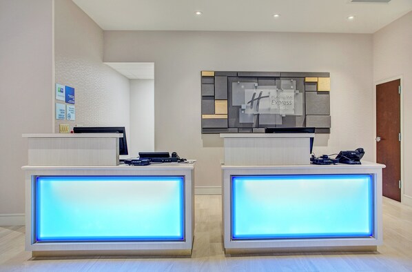 A reception desk with a digital display, a wall-mounted sign, and a door in a hotel lobby.