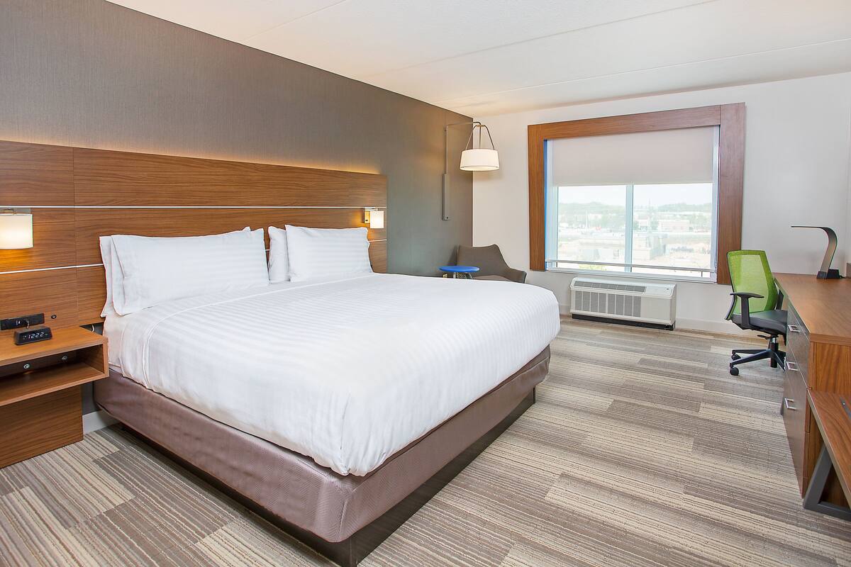 A hotel room with a large bed, a desk, a chair, and a television.