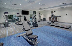 A gym with various exercise equipment including treadmills, elliptical machines, and a bench press.