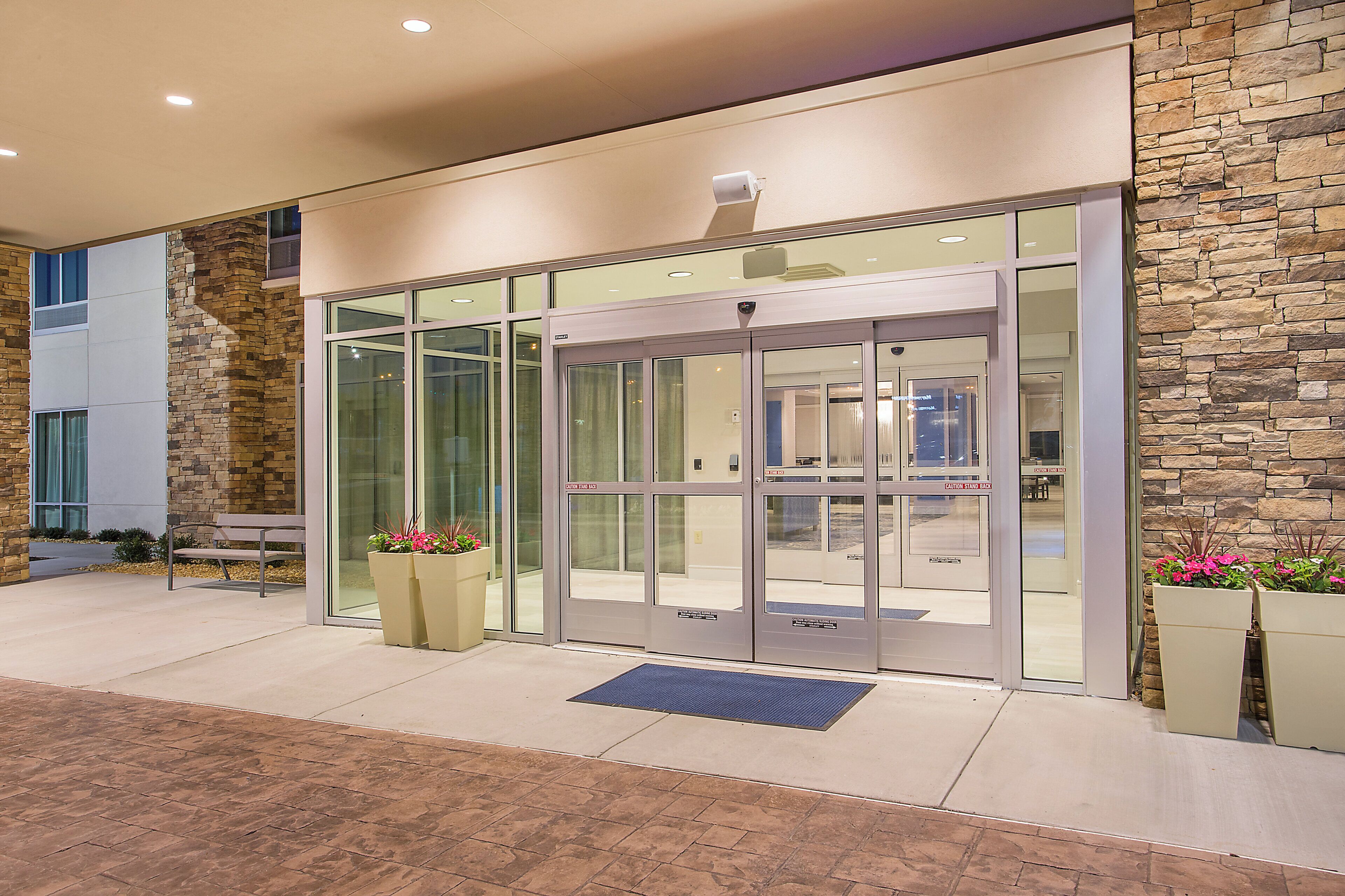 A modern building entrance with a revolving door, stone facade, and potted plants.