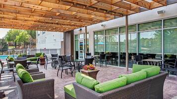 Un patio exterior con mobiliario de mimbre, una piscina y una zona de estar cubierta.
