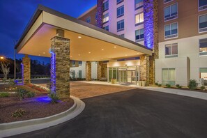 L’entrée d’un hôtel, avec une allée couverte, des piliers en pierre et une porte d’entrée en verre.
