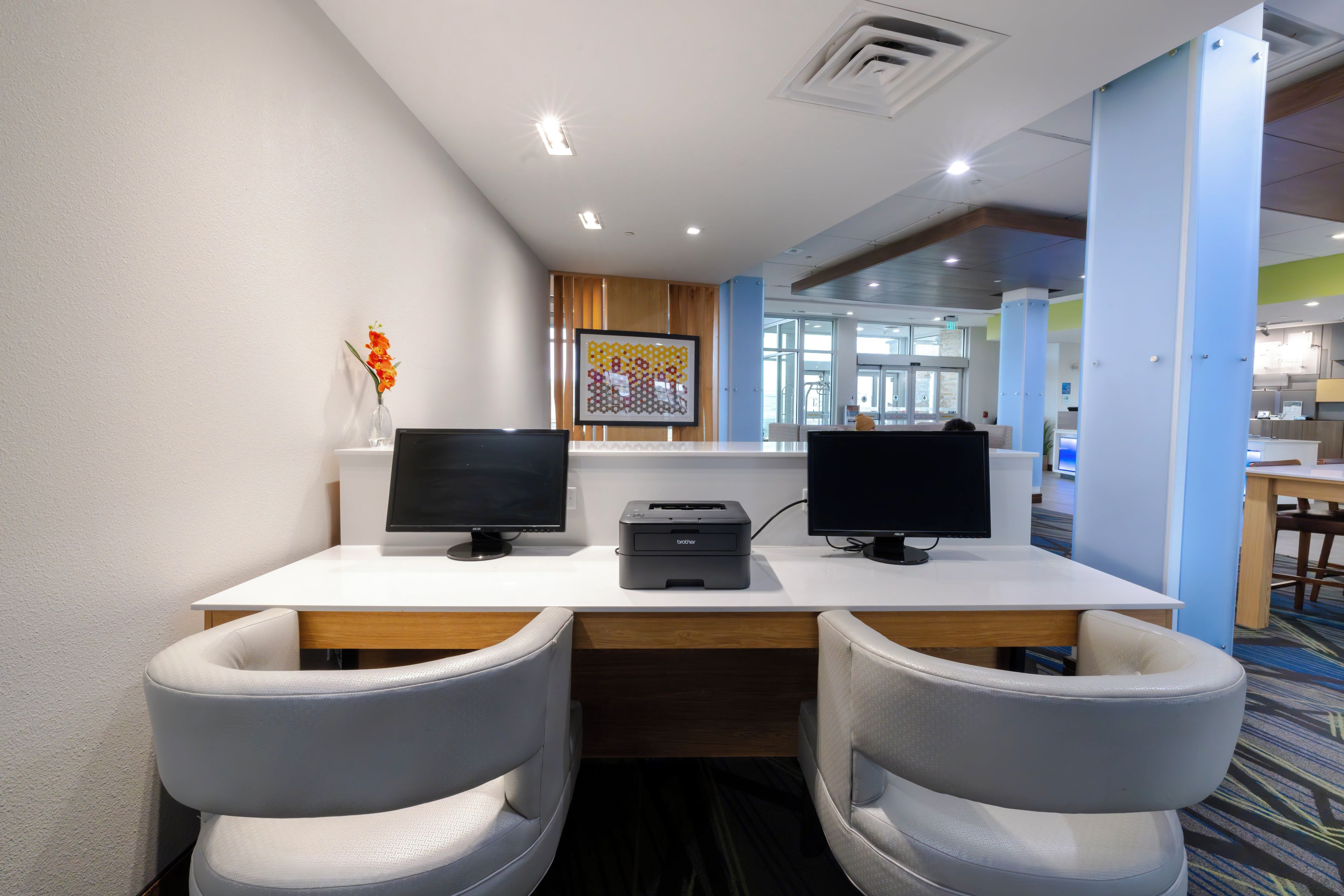 A reception desk with two monitors, a printer, and a vase with flowers.