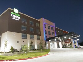 Edifício do Holiday Inn Express & Suites com design moderno, apresentando um telhado plano, várias janelas e uma área de entrada bem iluminada.