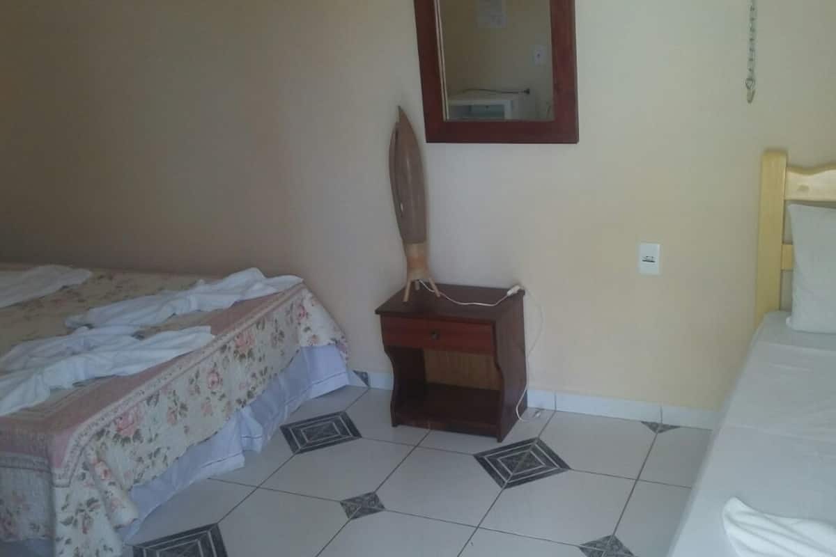 Une chambre avec deux lits, une table de chevet en bois, un miroir et un sol carrelé.