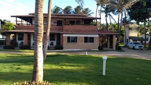 Una casa de dos pisos con fachada de ladrillo y techo de tejas, rodeada de un césped cuidado y palmeras.