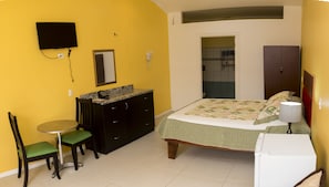 A compact bedroom with a bed, a desk, a chair, a TV, and a small kitchenette. - Apartamento El Descanso (Curridabat)