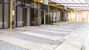 A covered outdoor area with a tiled walkway, potted plants, and a building with large glass doors. - Apartamento El Descanso (Curridabat)