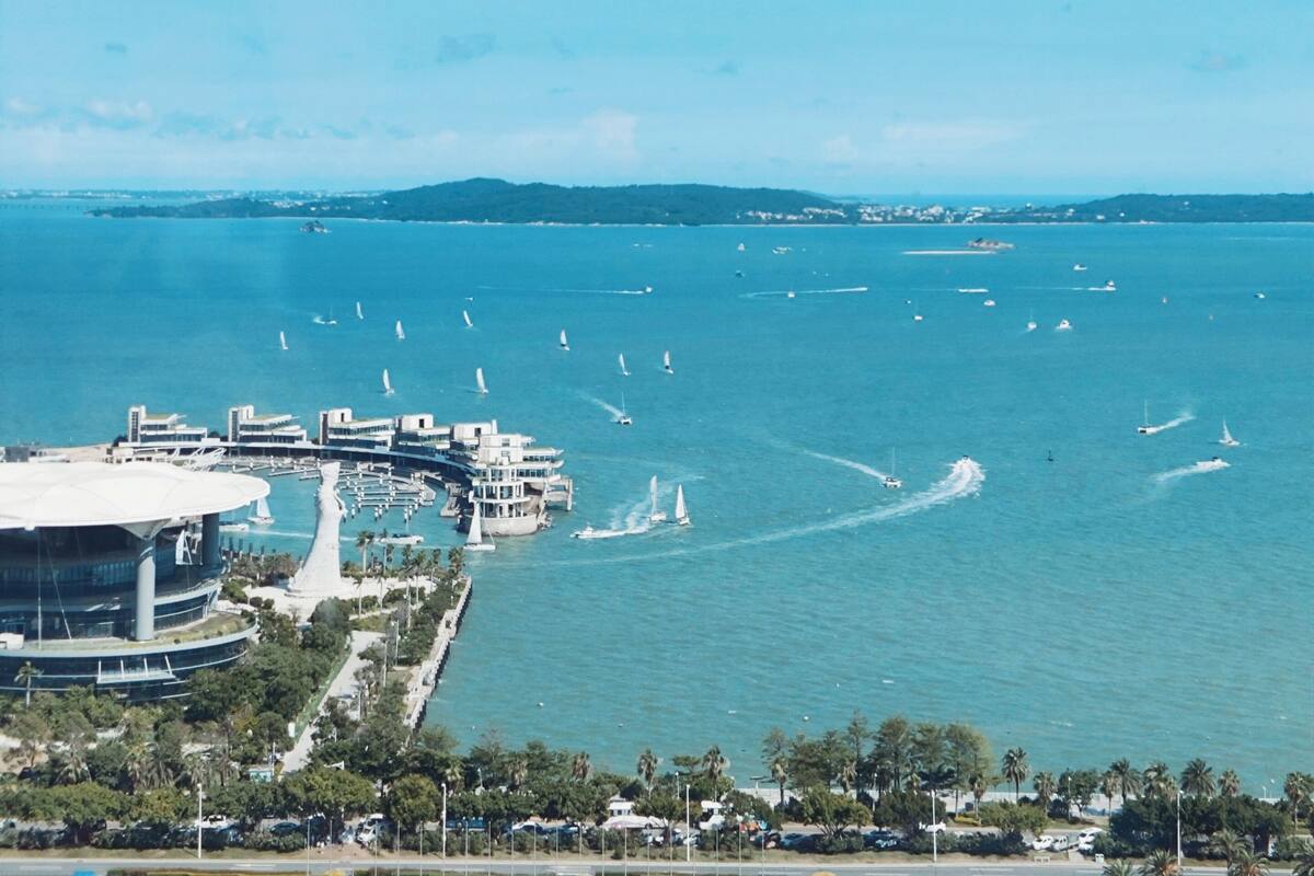 A coastal cityscape with a marina, sailboats, and modern buildings.
