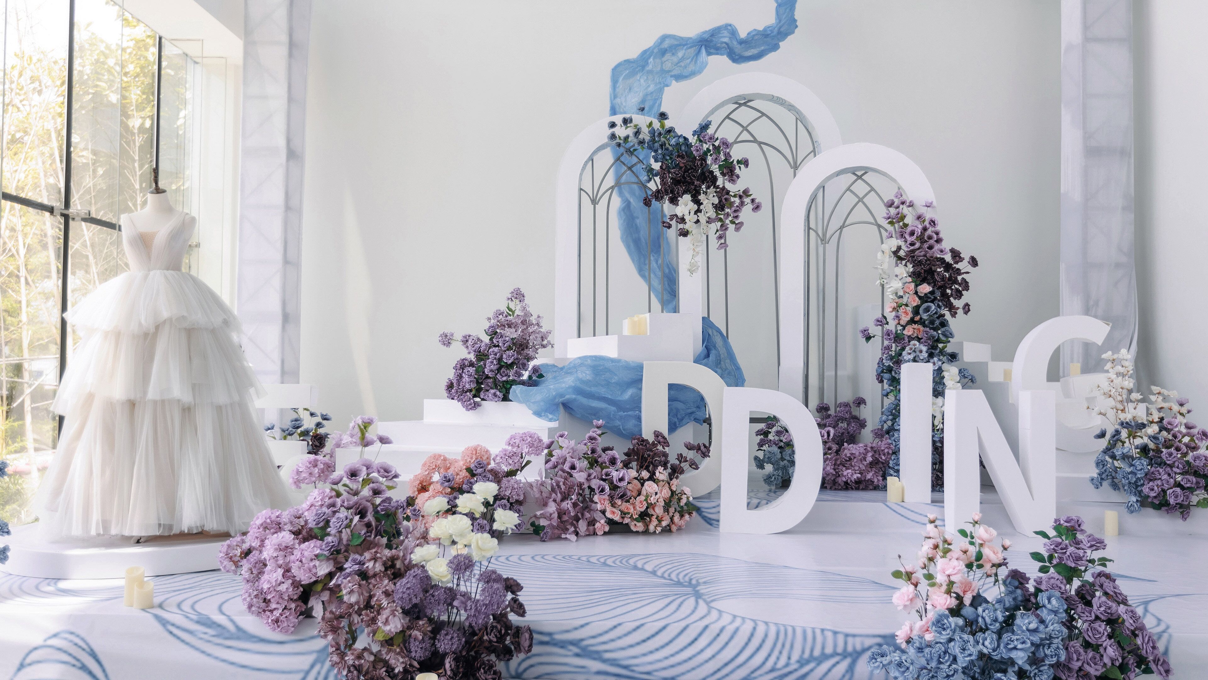 A wedding setup with a dress on a mannequin, floral arrangements, and large letters spelling 'WEDDING'.