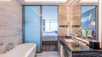 A modern bathroom with a large bathtub, a vanity with a mirror, and a view into the bedroom.