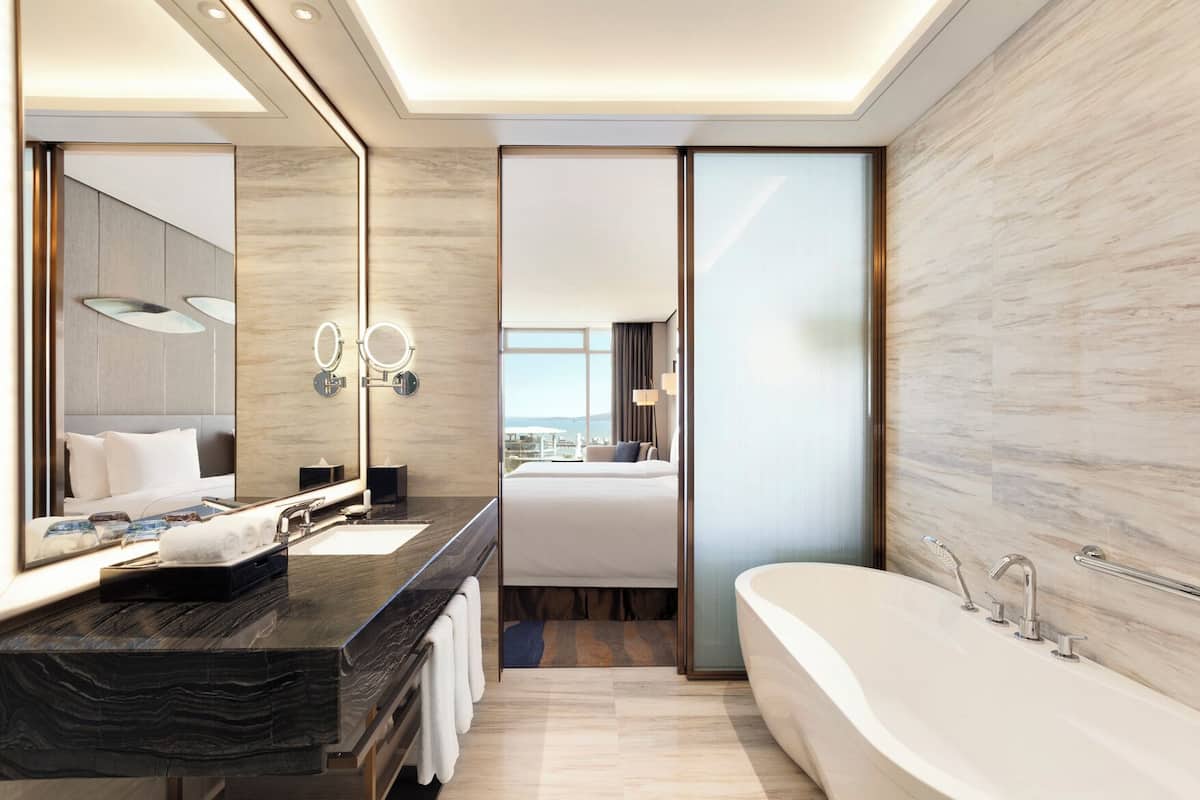 A modern hotel bathroom with a large bathtub, a double sink vanity, and a large mirror.