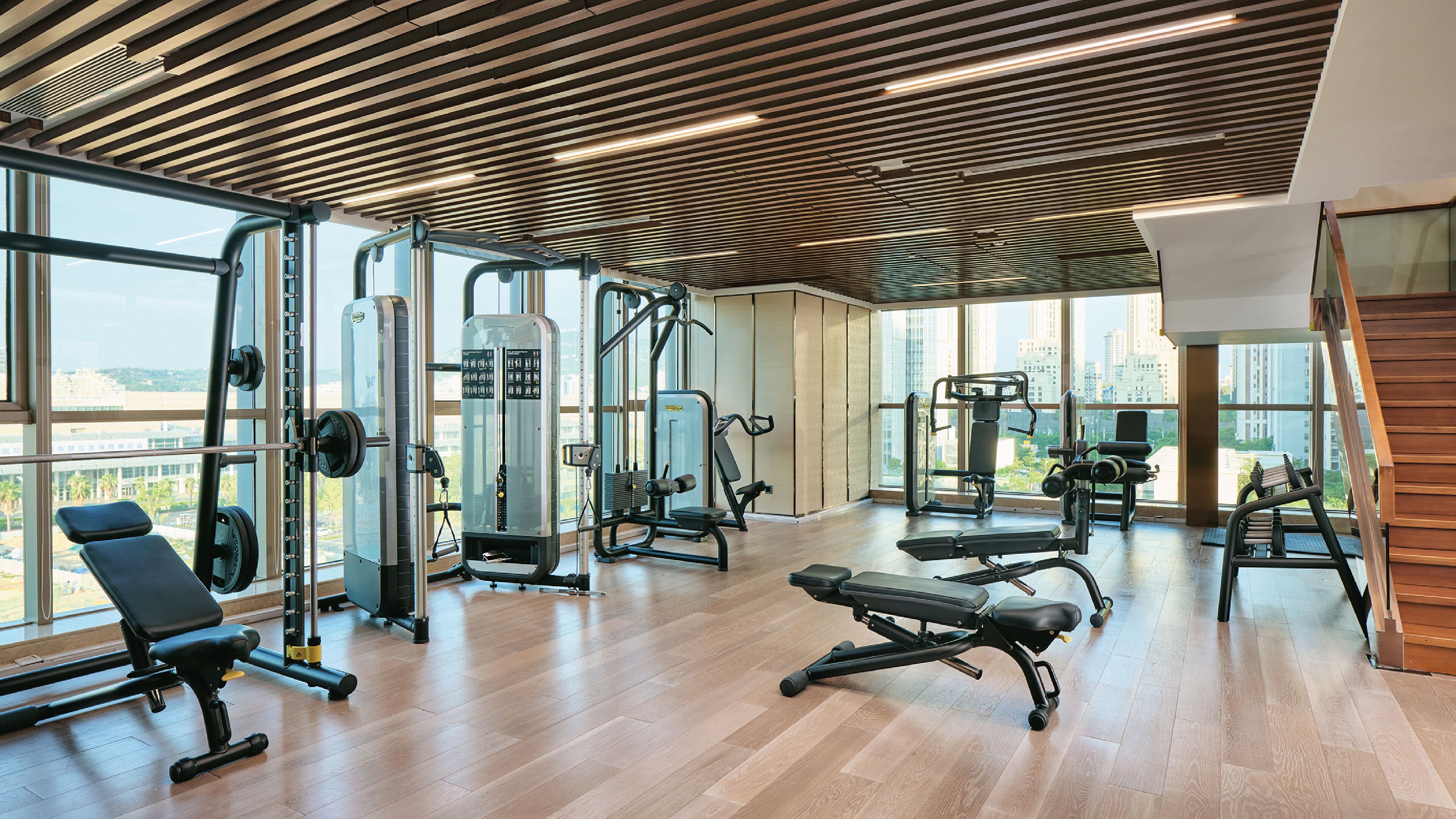 A gym with various exercise equipment, large windows, and a wooden ceiling.