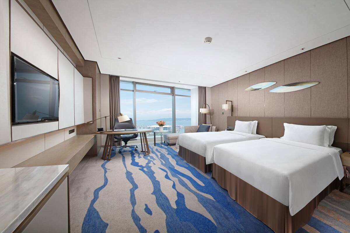 A hotel room with a large TV, two beds, a desk, and a view of the city.