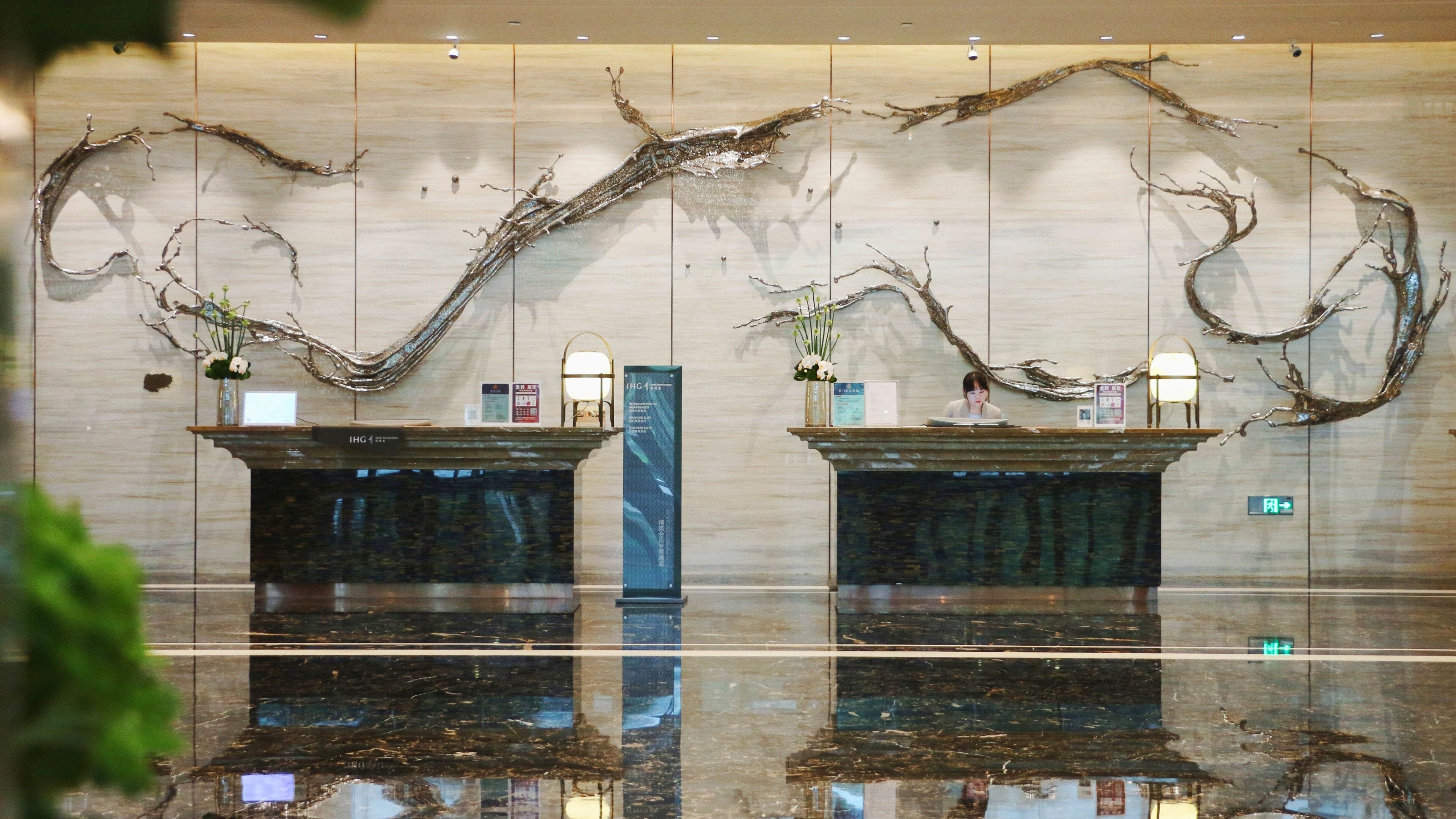 A reception desk with a marble counter, a blue vertical sign, and a wall with abstract tree branch decorations.