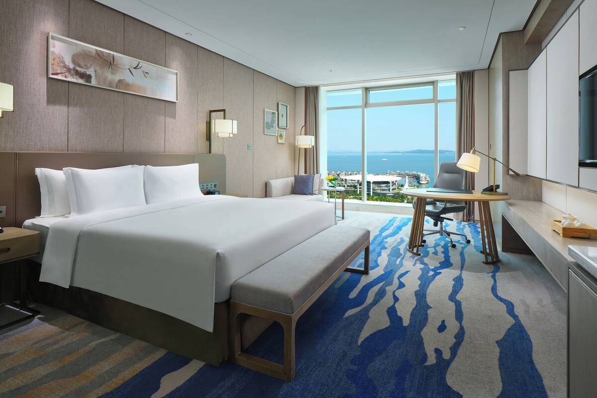 A hotel room with a large bed, a desk, and a view of the city.