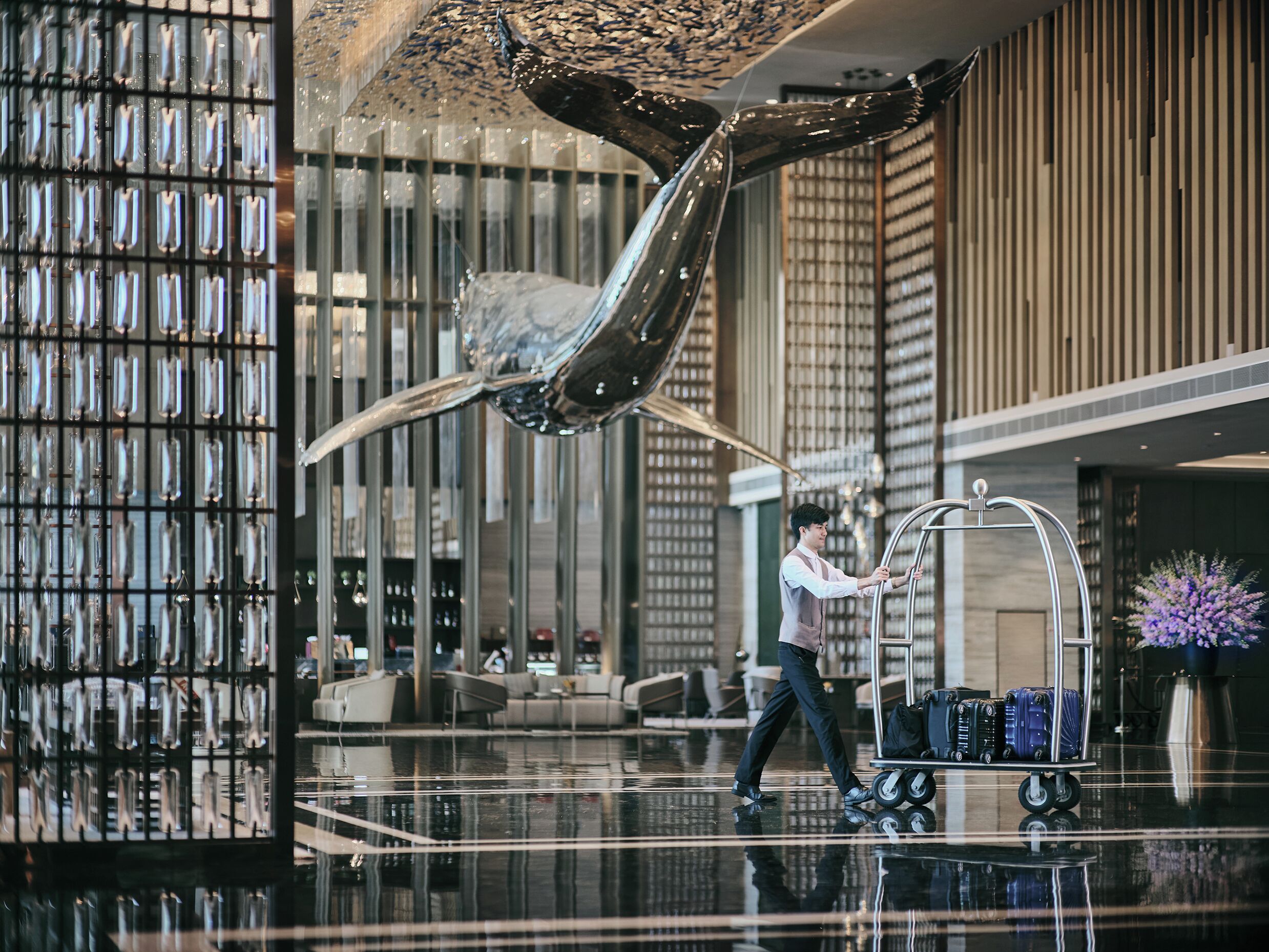 A modern lobby with a large metallic sculpture, a luggage cart, and a seating area.