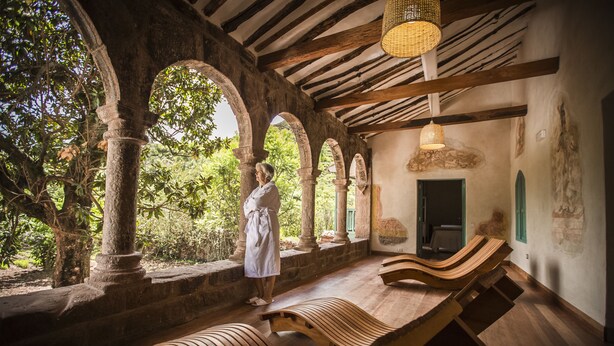 A spa area with wooden benches, stone columns, and a person in a robe. - Explora Valle Sagrado (Huayllabamba)
