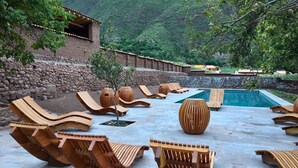 A poolside area with lounge chairs and wooden planters arranged around a swimming pool. - Explora Valle Sagrado (Huayllabamba)