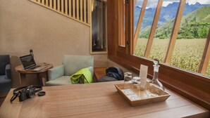 A room with a wooden table, a laptop, a camera, and a window with a view of a mountainous landscape. - Explora Valle Sagrado (Huayllabamba)