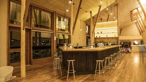 A bar area with wooden beams, large windows, and bar stools. - Explora Valle Sagrado (Huayllabamba)