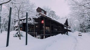 A log cabin with a snow-covered roof and a visible 'illy' sign, surrounded by snow-laden trees. - Double Black Hotel (Hakuba)