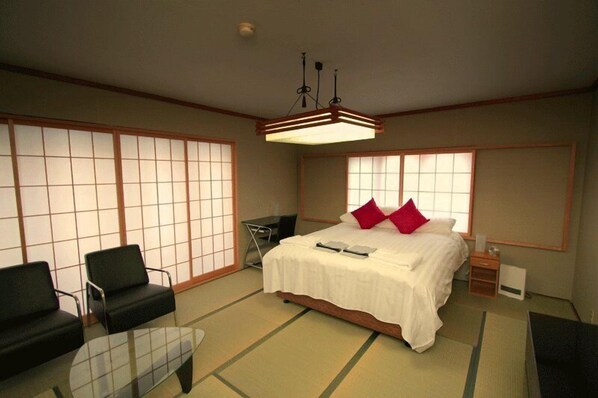 A traditional Japanese-style room with tatami flooring, a bed with white bedding, a desk, and a chair. - Double Black Hotel (Hakuba)