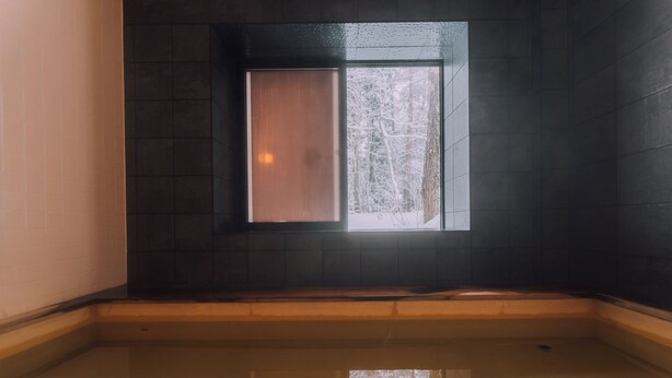 A corner room with a small window, a wooden bench, and a tiled floor. - Double Black Hotel (Hakuba)