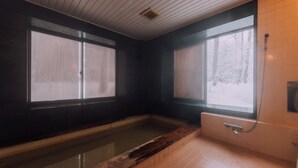 A room with a wooden bathtub, large frosted windows, and a view of a snowy forest. - Double Black Hotel (Hakuba)