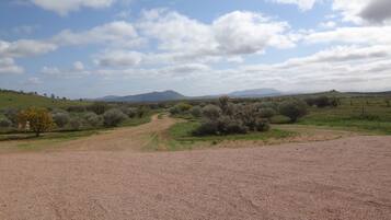 A gravel path leading through a dry, open landscape with sparse vegetation and distant mountains under a partly cloudy sky.