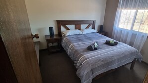 A neatly made bed with a striped bedspread, a wooden headboard, and a bedside table with a lamp. - Windana Cottages (Hawker)