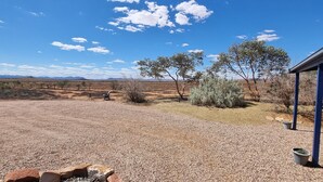 A gravel patio with a covered seating area, a small fire pit, and sparse vegetation. - Windana Cottages (Hawker)
