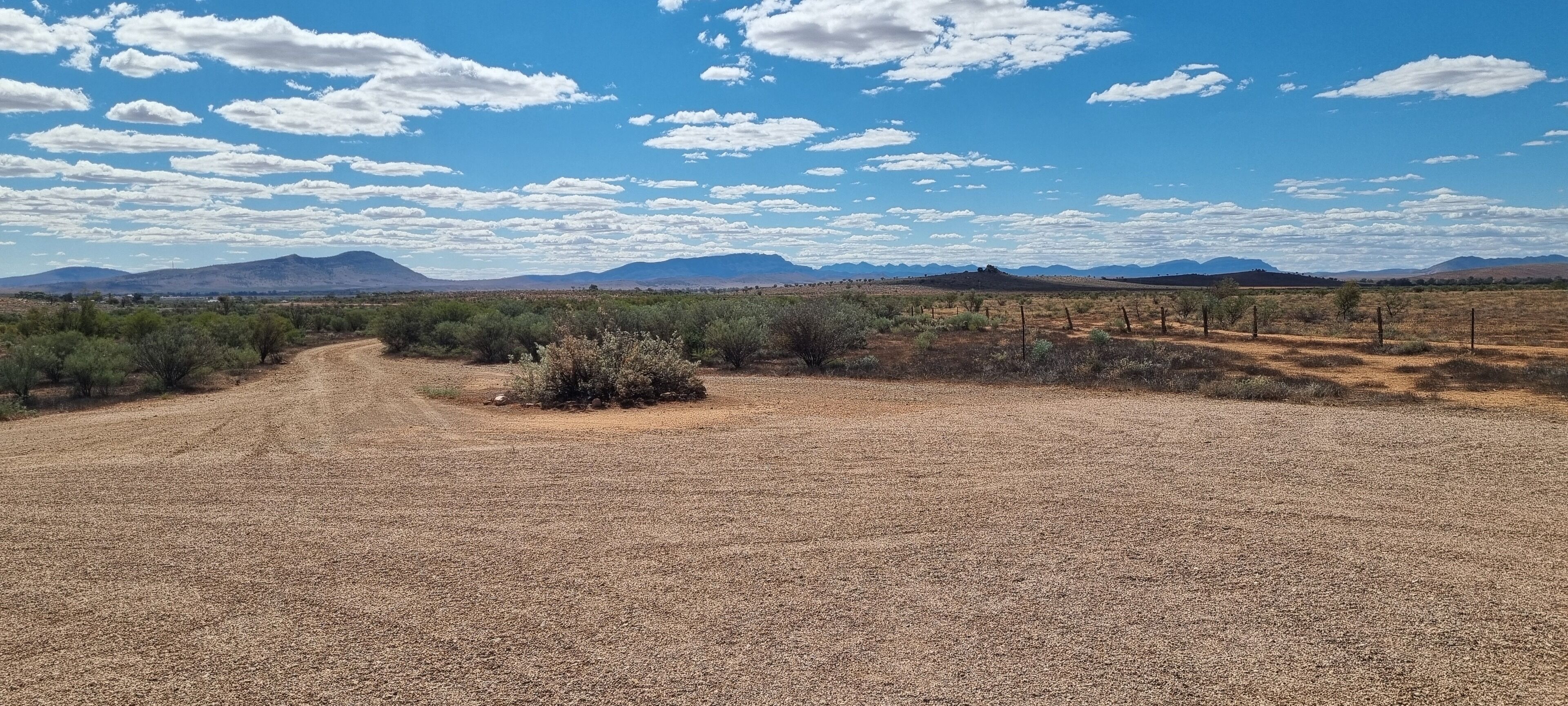 A dry, open landscape with sparse vegetation and distant mountains under a partly cloudy sky.