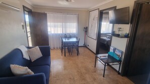 A compact living space with a sofa, a dining table, and a small TV. - Windana Cottages (Hawker)