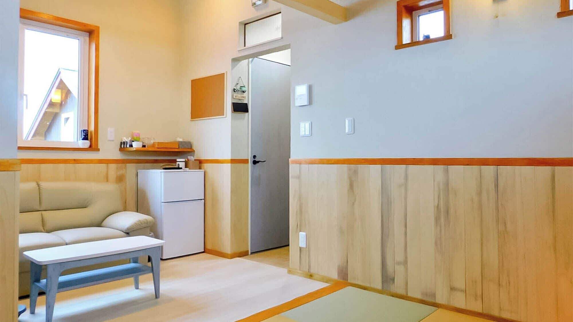 A compact room with a sofa, a small table, a refrigerator, and a door leading to another room.