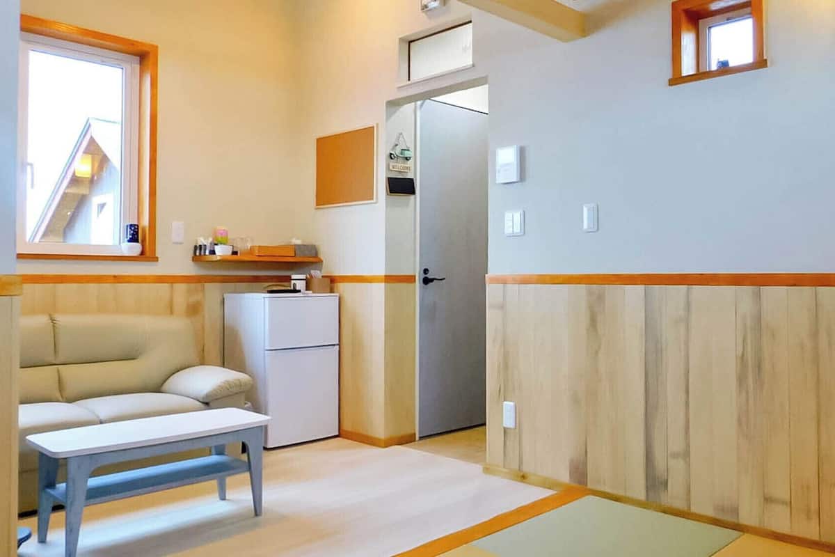 Ein kleines Zimmer mit einer Couch, einem Tisch, einem Kühlschrank und einer Tür zu einem weiteren Raum.