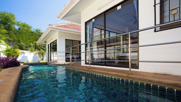 A swimming pool adjacent to a building with large windows and a tiled deck.