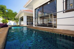 A swimming pool adjacent to a building with large windows and a tiled deck. - Magic Villa Pattaya (Pattaya)