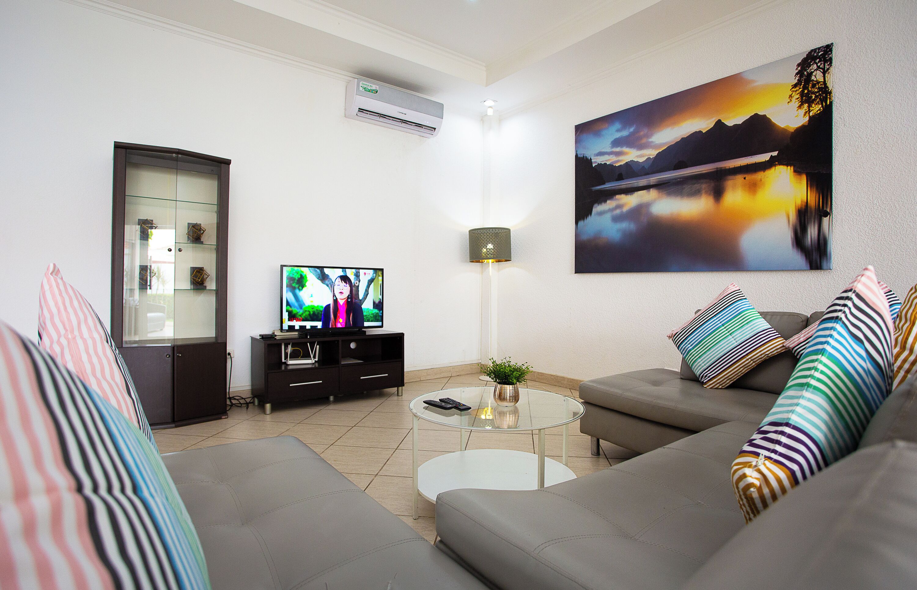 A modern living room with a sofa, a glass coffee table, a television, and a painting of a landscape.
