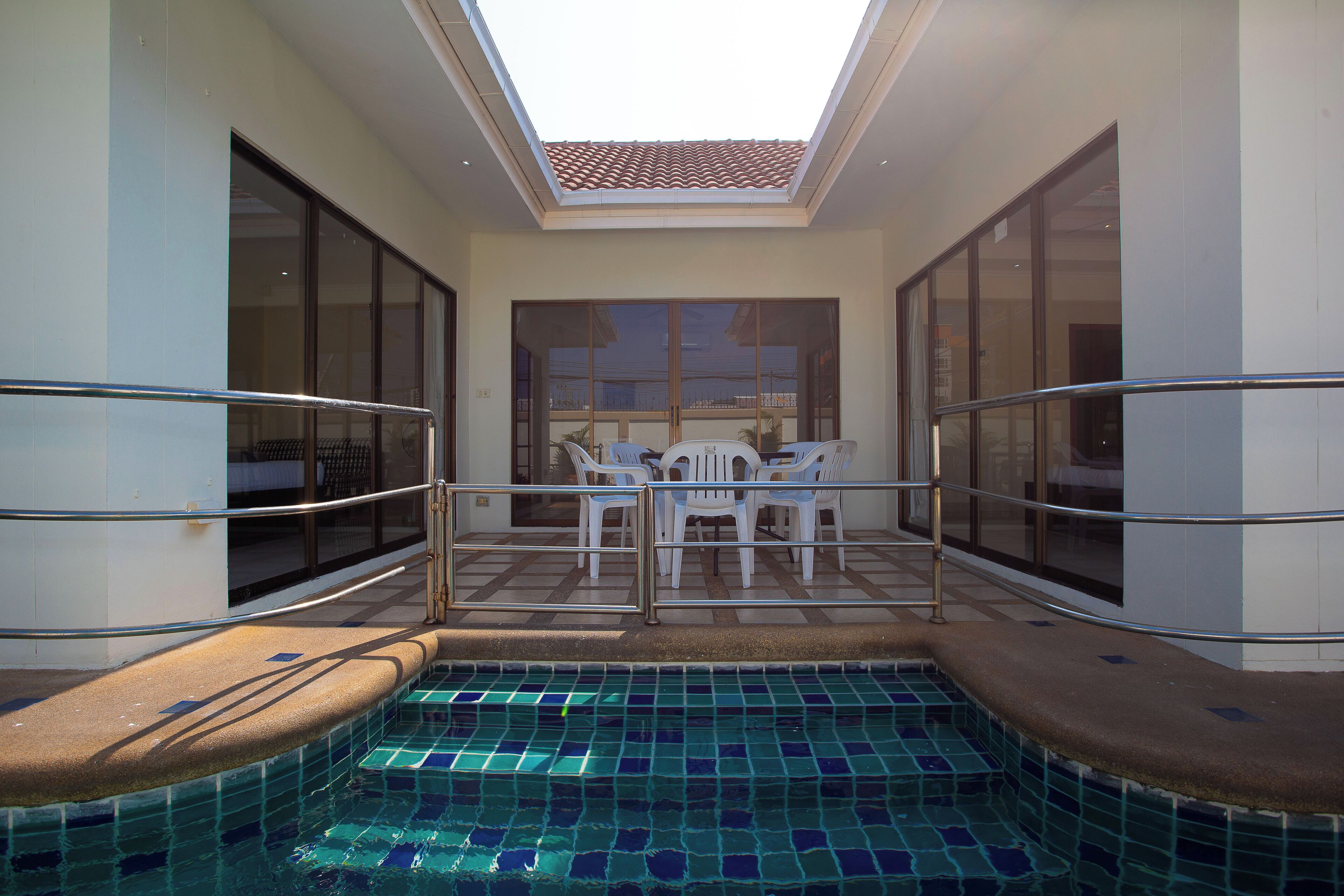 A small indoor pool with a tiled floor and a glass ceiling, surrounded by glass walls and a metal railing.