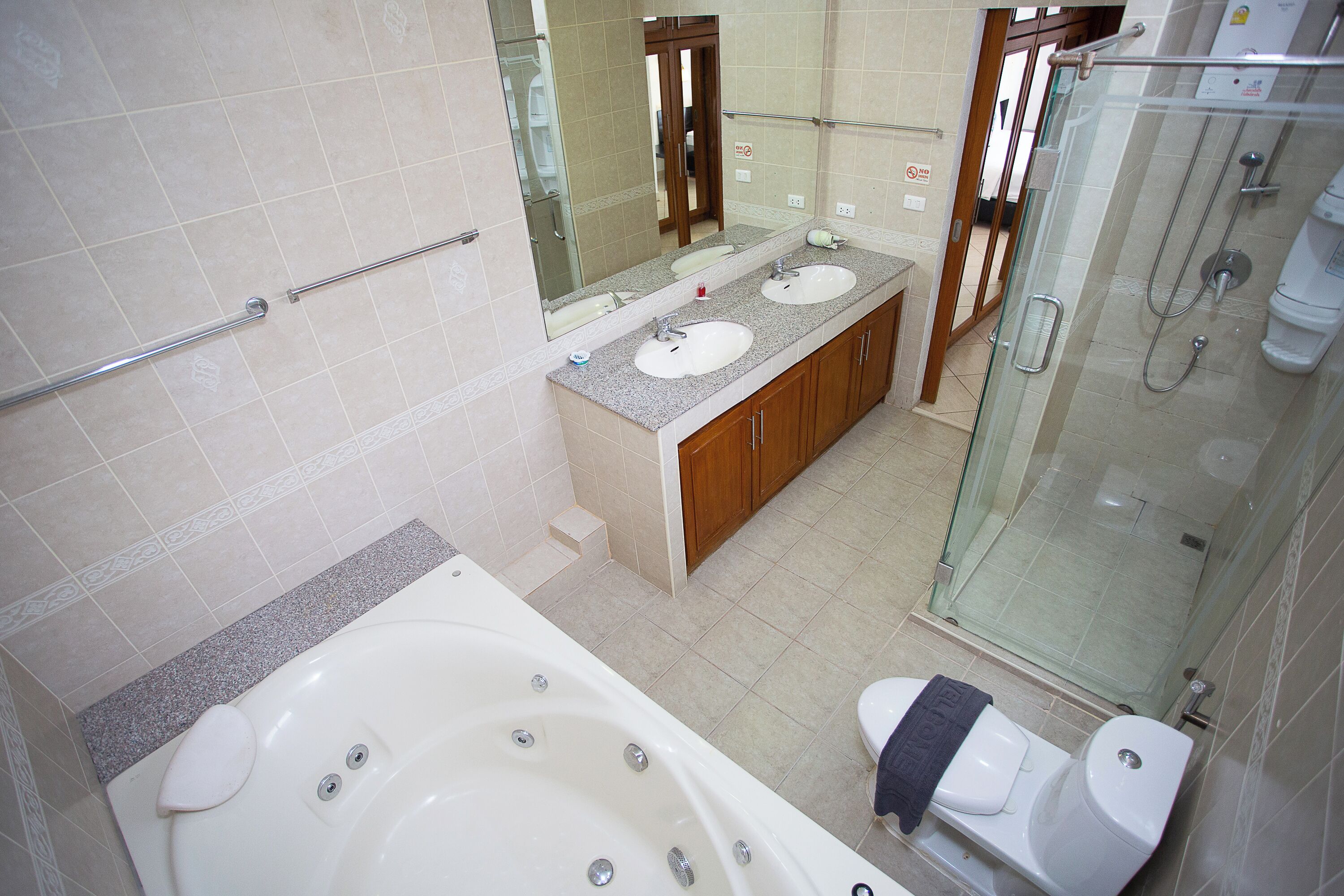 A bathroom with a large bathtub, two sinks, a glass-enclosed shower, and wooden cabinets.