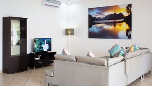 A modern living room with a grey sofa, a flat-screen TV, a cabinet, and a large landscape painting on the wall.